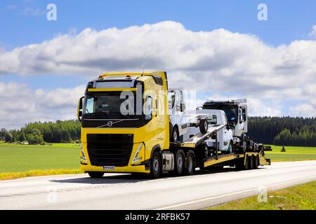 Neuer gelber Lkw Volvo FH 500 transportiert an einem Sommertag drei neue leichte Lkw auf der Autobahn. Jokioinen, Finnland. 21. Juli 2023. Stockfoto