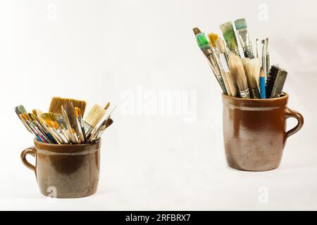 Künstlerische Pinsel und Malwerkzeuge in alten Ton/Keramik Töpfen auf weißem neutralen Hintergrund. Stockfoto