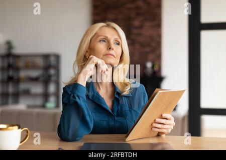 Porträt einer pensiven, reifen Frau, die zur Seite blickt und denkt, über Probleme nachdenkt, im Wohnzimmer sitzt, Kopierraum Stockfoto