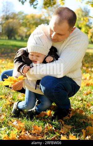 Familienwochenende im Herbstpark. Der Vater zeigt dem kleinen Sohn gelbe Blätter, aber das Baby ist unartig und weint. Vertikales Foto Stockfoto