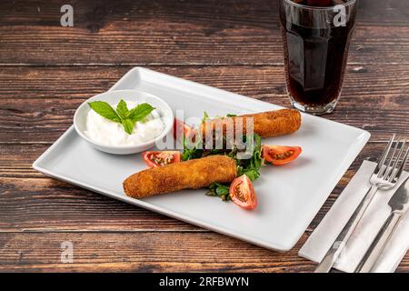 Mozzarella-Stäbchen mit Grün und Sauce auf einem weißen Porzellanteller Stockfoto