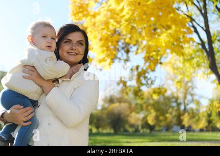 Die junge, stilvolle Mutter hält das Kind in ihren Armen und umarmt sich in einem Herbstpark. Mutter in weißer Jacke und ein Junge in Strickpullover. Konzept: Mutter Stockfoto