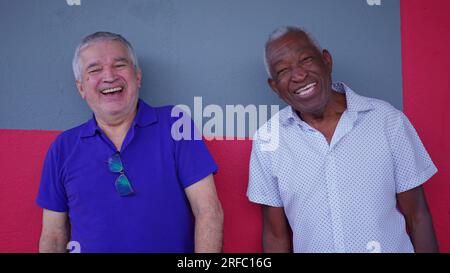 Alte Freundschaft von zwei verschiedenen Senioren, die auf der Straße stehen und lächeln, während sie miteinander interagieren Stockfoto