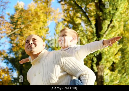 An einem sonnigen Herbsttag haben Sohn und Vater viel Spaß beim Flugzeugspielen im Freien. Horizontales Foto Stockfoto