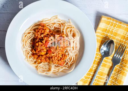 Eine Schüssel Ragu Bolognaise, serviert auf einem Bett mit Spaghetti. Eine Portion wird auf einen Tisch in einer tiefen weißen Schüssel gestellt Stockfoto