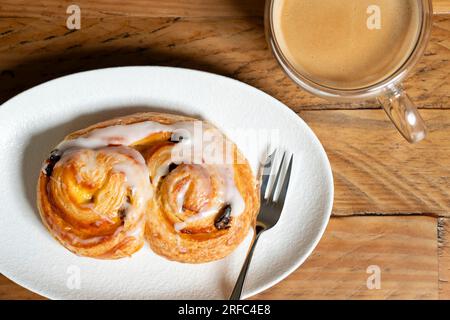 Ein dänisches Zitronengebäck, serviert an einem Tisch auf einem Teller mit einer Konditorgabel. Dazu gibt es eine frisch gebrühte Tasse Kaffee. Stockfoto