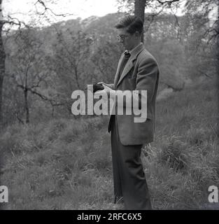 1950er Jahre, historisch, Mann in einer Sportjacke, der in einem bewaldeten Hügel steht und eine Amsel hält, möglicherweise verletzt, England, Großbritannien. Stockfoto