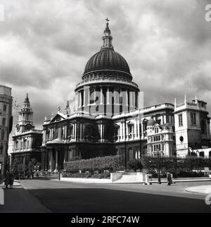 1950er Jahre, historisch, nach dem 2. Weltkrieg und eine rußbedeckte St. Pauls Cathederal, von der Seite und von hinten gesehen, auf dem St Paul's Churchyard, London, England, Großbritannien. Das von Christopher Wren entworfene Gebäude befindet sich auf dem Ludgate Hill am höchsten Punkt der City of London, wo die berühmte Kuppel die Skyline dominiert. Das Gebäude übertrug auf wundersame Weise den Blitz von 1940 im Zweiten Weltkrieg. Die anglikanische Kirche ist Sitz des Bischofs von London. Stockfoto