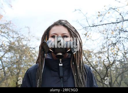 Porträt einer Frau in einer schwarzen Jacke mit Dreadlocks und einer Gasmaske mit Stacheln. Eine Frau, die im Herbstpark posiert. Horizontales Foto Stockfoto