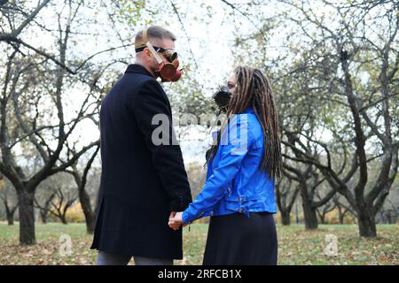 Eine Frau mit Dreadlocks und einer Gasmaske hält die Hand eines Mannes mit einer Steampunk-Brille und einer Gasmaske. Liebe in einer ökologischen Katastrophe. Horizontales Foto Stockfoto