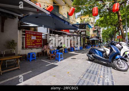 Hanoi, Vietnam - 28. Mai 2023: Eine lebendige Straße lädt zum Leben ein, wenn sich die Einheimischen in einem belebten Restaurant am Straßenrand versammeln. Sie sitzen auf niedrigen Hockern und lachen gemeinsam Stockfoto