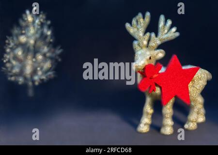 Goldene, glänzende Rentierfigur mit einem weihnachtsbaum auf dunklem Hintergrund. Weihnachtshintergrund/Karte, Geschenkkarte, roter Stern – Anhänger/Anhänger. Stockfoto