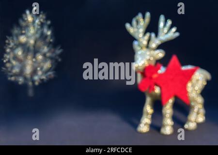 Bokeh-weihnachtshintergrund. Goldene, glänzende Rentierfigur mit einem weihnachtsbaum auf dunklem Hintergrund. Weihnachtshintergrund/Karte, Geschenkkarte, roter Stern Stockfoto