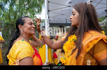 Vor der Feuerspaziergang-Zeremonie auf dem spirituellen Arya-Gelände... legt eine attraktive Hindu-Frau einer älteren Frau eine Tilaka auf die Stirn. In Queens. Stockfoto