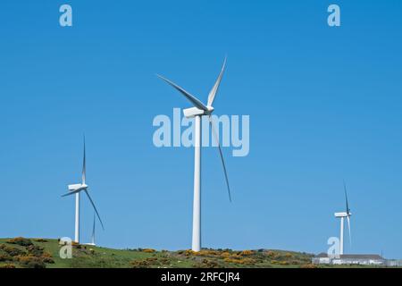 Wenn man die Zufahrtsstraße zum Windpark Ardrossan mit seinen Windturbinen vor dem Hügel hinaufblickt, sind die Windturbinen aufgrund des fehlenden Winds statisch Stockfoto