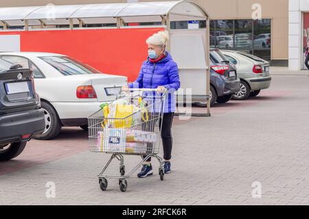 Foto einer reifen Frau, die eine Schutzmaske mit Einkaufswagen auf dem Parkplatz während der Coronavirus-Pandemie trägt. Alltag, Kopierraum. Stockfoto