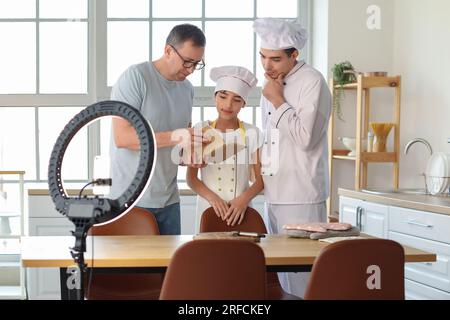 Glücklicher kleiner Junge mit seinem Vater und Großvater, der Kochvideo in der Küche aufnimmt Stockfoto