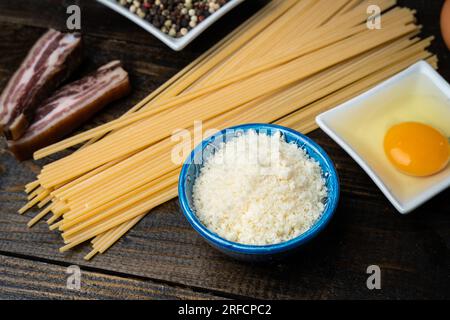 Italienische Pasta Spaghetti Carbonara Zutaten, Pfeffer, Käse, Eier und Speck auf dunklem Holzhintergrund Stockfoto