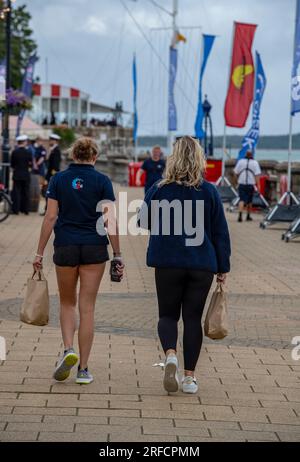 Zwei junge Frauen spazieren entlang der Parade bei cowes auf der Isle of wight während der jährlichen cowes Week Yachting und Seeleute Regatta. Jachtfrauen laufen. Stockfoto