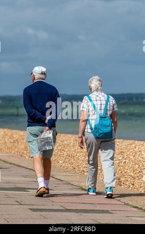 Ein älteres Paar, das zusammen am Meer spaziert. Ein Paar im Ruhestand, das an der Promenade entlang spaziert oder an der Promenade von cowes auf der Insel wight uk entlang läuft. Stockfoto