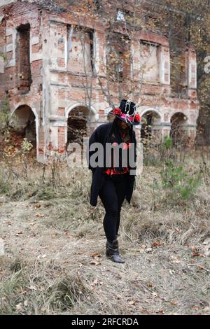 Eine Frau im Bild von Baron Saturday posiert vor dem Hintergrund eines alten Backsteingebäudes. Das Model trägt ein Korsett, eine Strickjacke und einen Hut Stockfoto