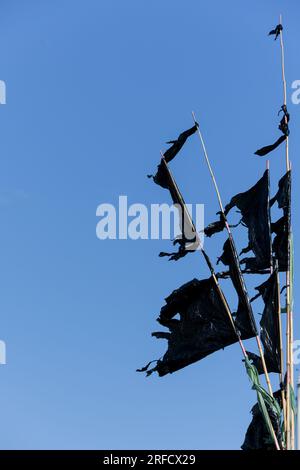 Mehrere schwarze Flaggen Wimpel, die mit Müllsäcken an Bambusstangen befestigt sind, als Marker für Fischernetze im Meer gegen blauen Himmel als Konzept für f Stockfoto