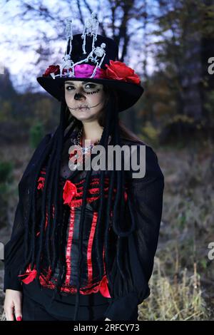 Eine Frau als Baron Saturday posiert für die Kamera. Das Model trägt ein Korsett, eine Strickjacke und einen mit Skelett verzierten Zylinderhut Stockfoto