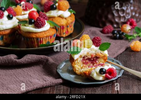 Cupcakes mit Buttercreme und Himbeer-Quark, dekoriert mit Beeren auf einer Holzfläche. Stockfoto