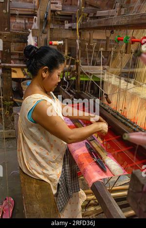 Frau, die in Sualkuchi, einer kleinen Stadt in Assam, das Zentrum der Seidenweberei, Seide auf einem Webstuhl webt. Stockfoto