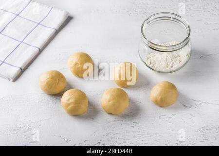 Ich koche hausgemachte Brötchen. Rohe Teigstücke oder Brötchen und ein Glas Mehl auf hellblauem Hintergrund. Stockfoto