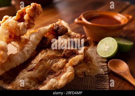 Chicharron. Knusprig gebratene Schweineschale, sind Stücke gefratener und gebratener Schweinehaut, traditionelle mexikanische Zutaten oder Snack serviert mit Limettensaft und roter Hure Stockfoto