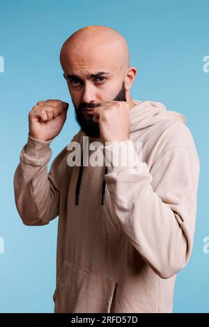 Ein arabischer Mann in Boxposition, der vor die Kamera schaut, bereit zum Kampf. Ein echter Kämpfer trägt einen legeren Hoodie mit geballten Fäusten und einem wilden Gesichtsausdruck-Studio-Porträt Stockfoto