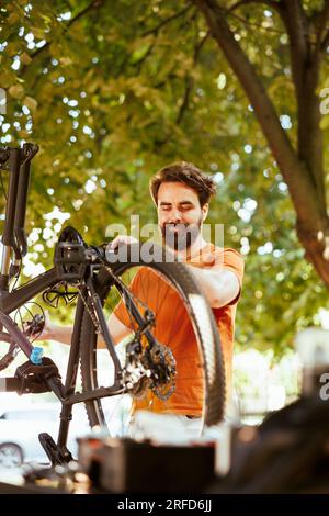 Begeisterter männlicher Radfahrer, der Fahrräder im Hof pflegt und pflegt. Engagierter, sportlicher, weißer Mann, der das Fahrrad für die Freizeit im Freien inspiziert und instand hält. Stockfoto