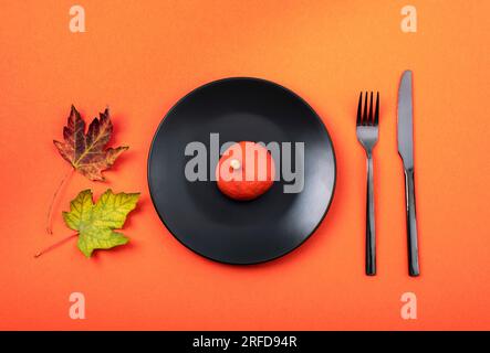 Herbsttisch mit schwarzer Platte und Kürbis auf orangefarbenem Hintergrund. Thanksgiving, halloween-Dekoration. Draufsicht, flach liegend. Stockfoto