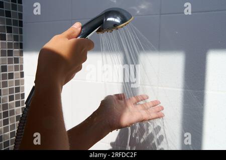 Weibliche Hand, die Wasser aus einem Regenduschkopf berührt, um die Wassertemperatur zu prüfen Stockfoto