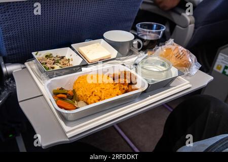 An Bord des Flugzeugs wird asiatisches Essen serviert, bestehend aus Reis und scharfem Hähnchen, Vorspeise, Dessert, Brötchen und Rotwein Stockfoto