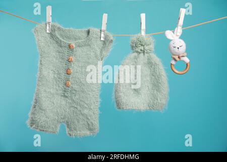 Gestrickte Babykleidung und handgemachtes Spielzeug trocknen an der Wäscheleine vor türkisfarbenem Hintergrund Stockfoto