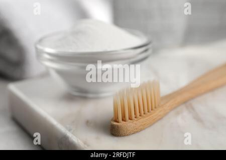 Bambuszahnbürste und Glasschüssel mit Backpulver auf Marmorbrett, Nahaufnahme. Platz für Text Stockfoto