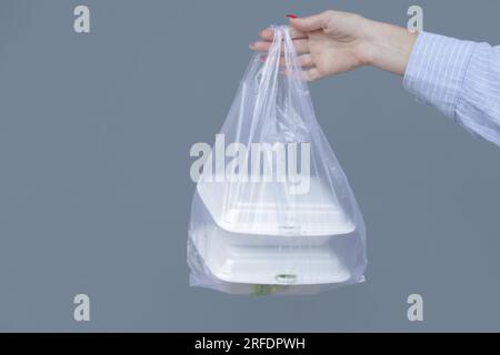 Frauenhände mit PVC-Plastiktüte und Lunchboxen aus Schaumstoff zum Mitnehmen. Einweg-Lebensmittelbehälter, Spendenkonzept. Stockfoto