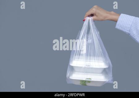 Frauenhände mit PVC-Plastiktüte und Lunchboxen aus Schaumstoff zum Mitnehmen. Einweg-Lebensmittelbehälter, Spendenkonzept. Stockfoto