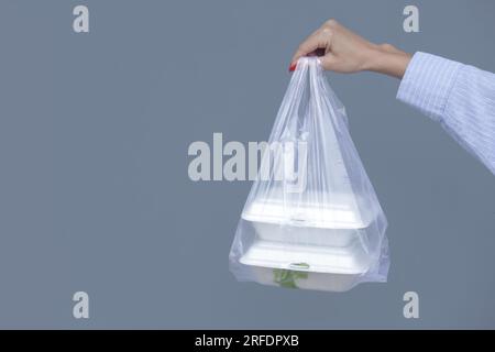 Frauenhände mit PVC-Plastiktüte und Lunchboxen aus Schaumstoff zum Mitnehmen. Einweg-Lebensmittelbehälter, Spendenkonzept. Stockfoto