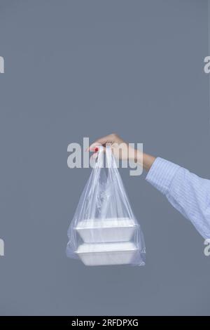 Frauenhände mit PVC-Plastiktüte und Lunchboxen aus Schaumstoff zum Mitnehmen. Einweg-Lebensmittelbehälter, Spendenkonzept. Stockfoto