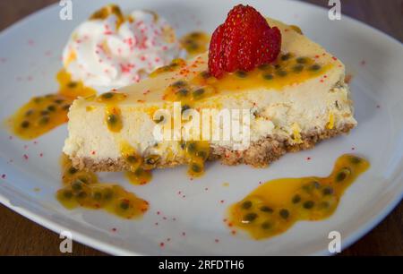 Ein Stück Passionsfrucht-Käsekuchen, garniert mit einer Erdbeere Stockfoto