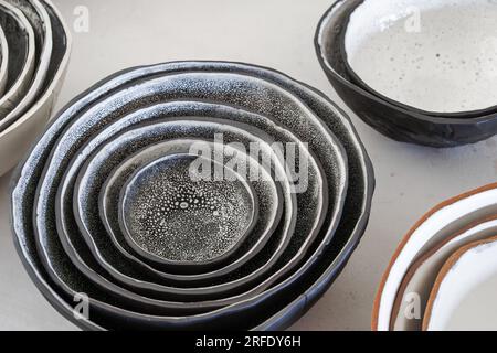 Eine Sammlung verschiedener handgemachter Tonschüsseln mit schwarz-weiß gesprenkelter Glasur und Terrakotta auf einem Tisch. Stockfoto