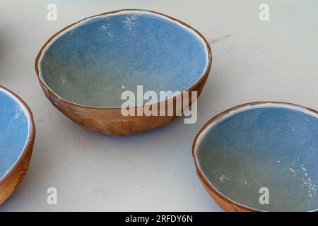Drei handgemachte braune und rote Terrakotta-Tonschalen mit blauer Glasur auf der Innenseite. Auf einem weißen Tisch. Stockfoto
