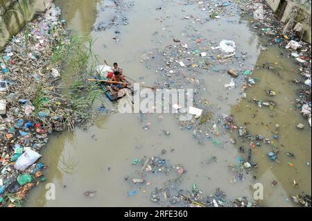 Ein Vater und Sohn rudern auf einem handgefertigten Floß und suchen nach Altkunststoff-Recyclingprodukten aus einem mit Kunststoffabfällen gefüllten Kanal im Kazir Bazar-Viertel von Sylhet. Dieser Kanal ist direkt mit dem Fluss Surma verbunden, der den Fluss Surma verschmutzt und das Flussbett füllt. Das Polyethylen hat sich in riesigen Haufen Schlamm angesammelt, was die Navigation behindert und zu einem Mangel an nutzbarem Wasser aus dem Surma-Fluss von Bangladesch führt. Sylhet, Bangladesch. Stockfoto