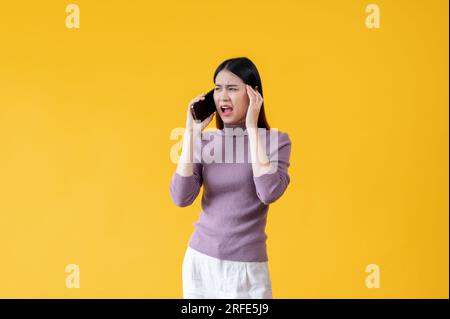 Eine gestresste und unglückliche Asiatin spricht aggressiv am Telefon, beschwert sich am Telefon über jemanden, ist unzufrieden. Isolierte Schreie Stockfoto