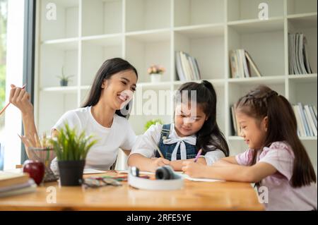 Eine schöne und nette asiatische Privatlehrerin unterrichtet junge Studenten in einem Café. Kindergarten, Grundschüler, Kinder, Babysitter, Te Stockfoto