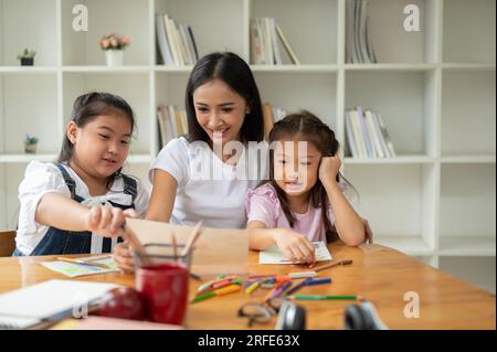 Eine glückliche und nette junge asiatische Babysitterin oder Privatlehrerin unterrichtet junge Kinder mit Kunst. Stockfoto