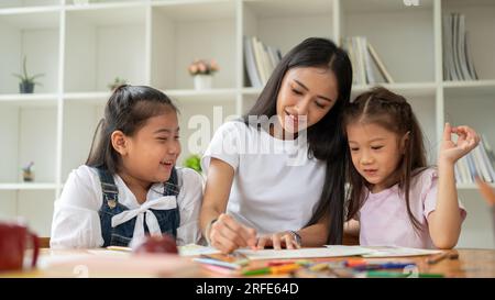 Eine nette asiatische Babysitterin oder Privatlehrerin unterrichtet junge Kinder in Kunst und zeichnet und malt gemeinsam. Kinder, Kindergartenkinder, Stockfoto